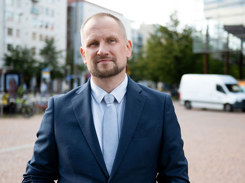 Katukuvassa mies katsoo kameraan. Takana pakettiauto.